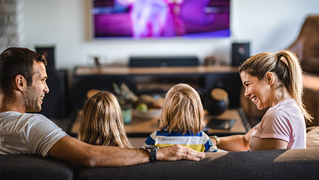 A family of four chatting and laughing in front of a television screen