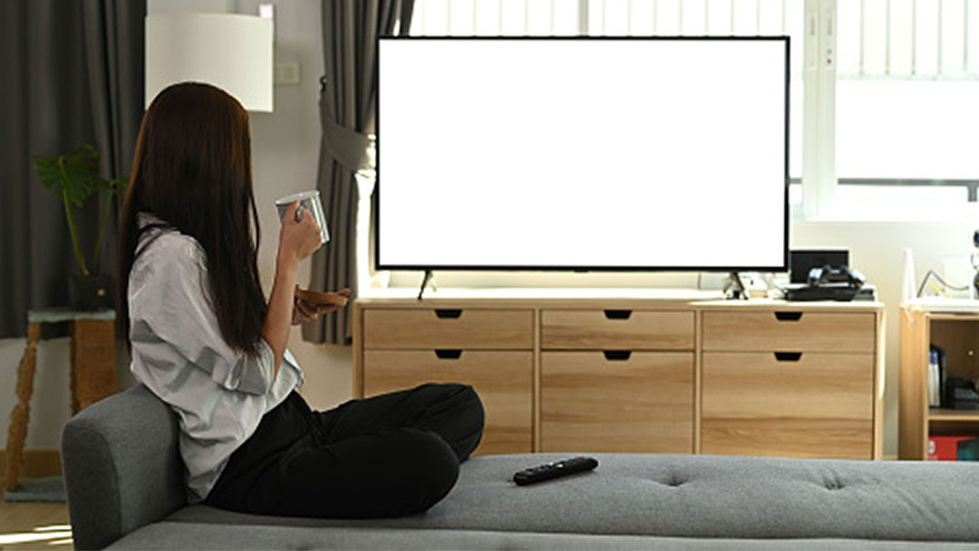 Woman sitting on a gray sofa with a coffee mug and watching television