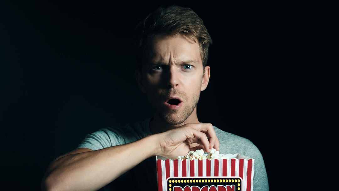 Man eating popcorn with a surprised look on face