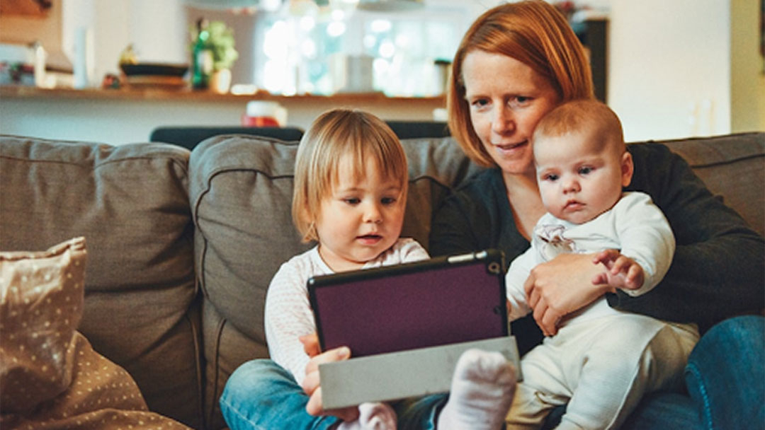 Mother sitting on the couch with her children and reading a tablet