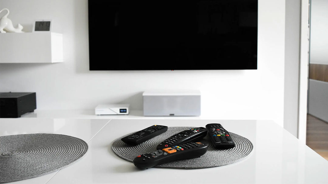 Multiple remotes in front of a TV screen in white room
