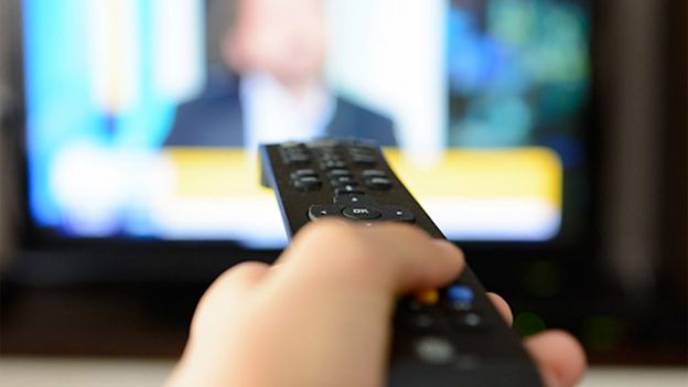 Hand clicking a remote control to change a channel on the television