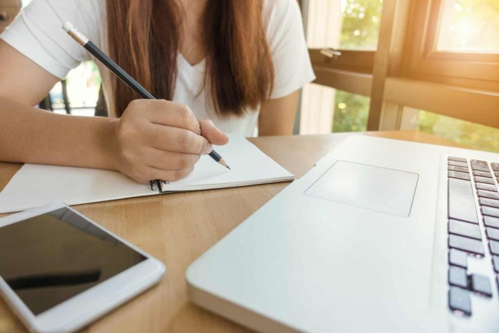 A student writing notes from her laptop. 