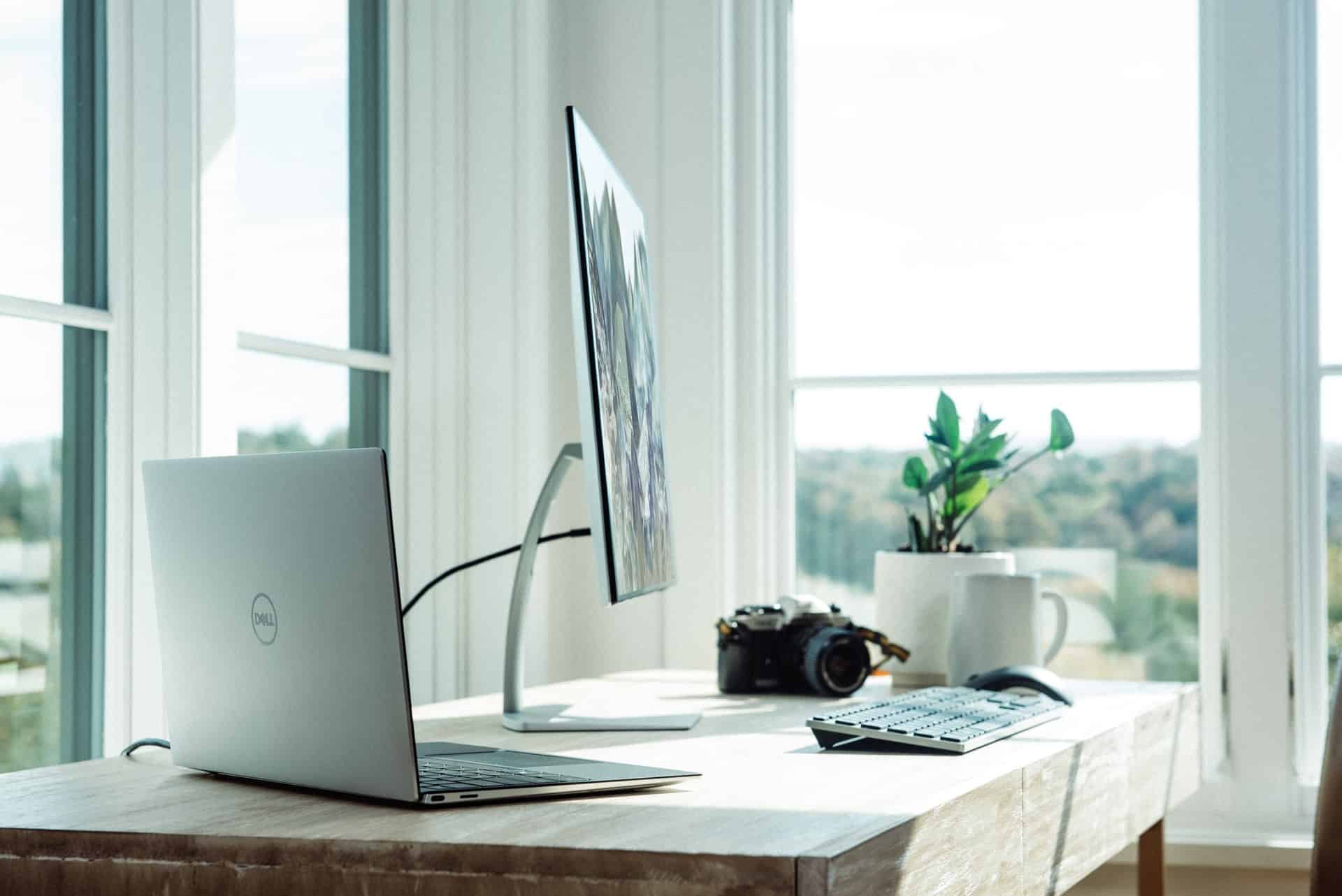 A large desktop and keyboard next to a laptop and camera