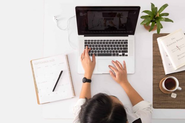 A woman working on her laptop with a calendar and a cup of tea.