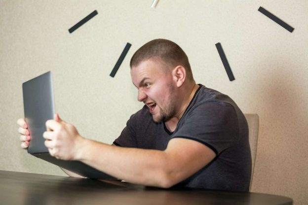 An angry man shaking his laptop