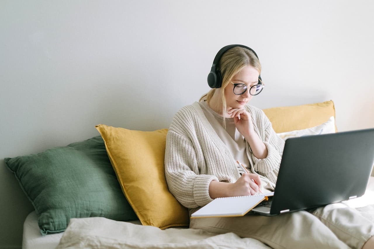 Woman writing on her laptop while wearing headphones