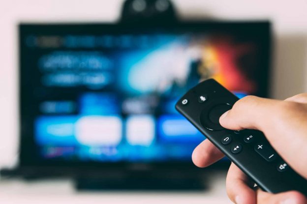 A person holding up A remote and streaming a show on tv