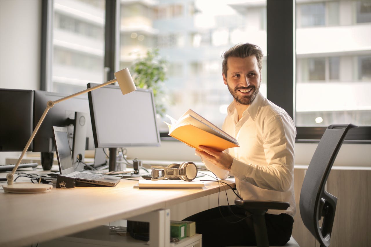 Man working at his desk with a book and a computer